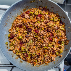 Ground beef for stuffing in a pan with olives, raisins, cranberries, walnuts, almonds, bay leaf and spices for Christmas dinner. Homemade traditional food concept