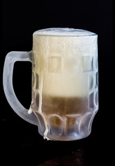 frozen beer glass with foam on black background