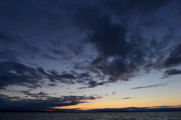Darkness and light in the twilight sky in the clouds above the water of the lake