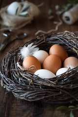 Easter celebration and preparation consept - Easter eggs in a nest on dark rustic wooden table with vintage scissors and a spool of jute twine for decoration