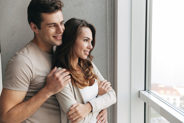 Happy lovely young couple standing at the window at home