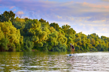 Stand up paddle boarding on Danube river at summer morning. Girl with perfect body on board