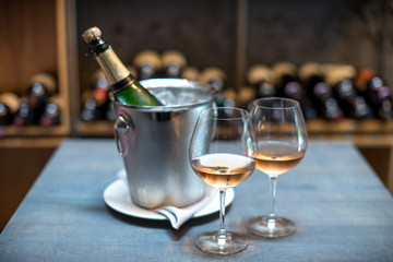 A bottle of champagne in a bucket with ice on the table. Two cold glasses of sparkling wine.