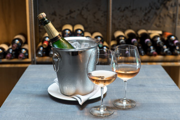 A bottle of champagne in a bucket with ice on the table. Two cold glasses of sparkling wine.