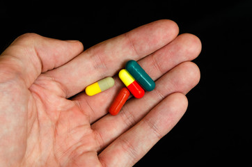 man holding a pill. Take a capsule. Medication.Black background.