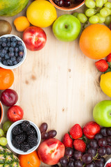 Rainbow fruits background circle frame, strawberries raspberries oranges plums apples kiwis grapes blueberries mango persimmon on light wooden table, top view, copy space for text, selective focus
