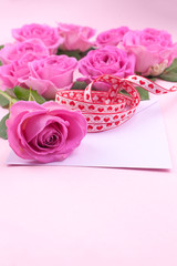 A bouquet of pink roses with petals on a pink background and a letter for text. Surprise in the concept of lovers day and mother's day. Flat lay. Copy space.