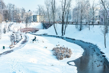 Fototapeta na wymiar panorama of a snowy city park with a river and a bridge