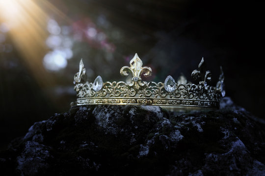 mysterious and magical photo of gold king crown over the stone covered with moss in the England woods or field landscape with light flare. Medieval period concept.