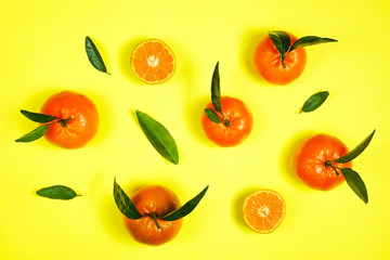 Close up image of juicy organic whole & halved tangerines with green leaves, visible core texture, isolated yellow background, copy space. Macro shot of bright citrus fruit slices. Top view, flat lay.