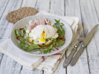 Healthy breakfast, sweet potatoes, cheese, avocado, ham, poached egg and greens with whole grain bread. Diet food. Breakfast served on a white plate on a light wooden table. Close up