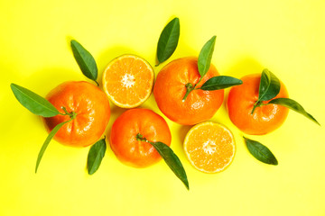 Close up image of juicy organic whole & halved tangerines with green leaves, visible core texture, isolated yellow background, copy space. Macro shot of bright citrus fruit slices. Top view, flat lay.