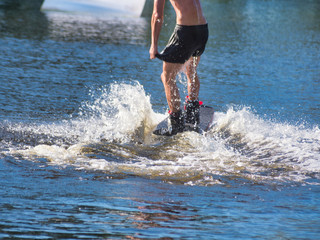 A wakeboarder, a young man on a wakeboard rides on the water in shorts without a t-shirt.