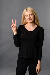 Happy beautiful woman showing victory sign and looking at camera. Friendly young lady.