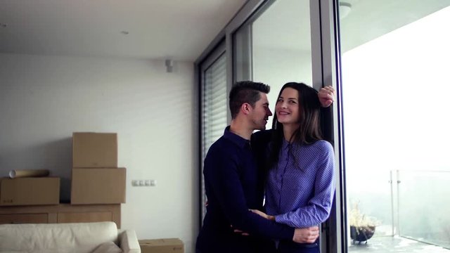 Young couple with cardboard boxes moving in a new home, hugging. Copy space.