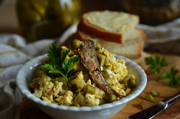 Egg paste with sprats in a white bowl on a wooden board