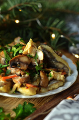 Baked fish with mushrooms on a white plate on a wooden disc sprinkled with parsley