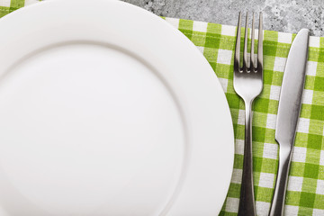 Fork, knife and white plate on green tablecloth with copy space, top view