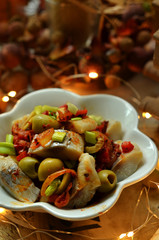 Herring with green olives and onion in a white bowl on a wooden background