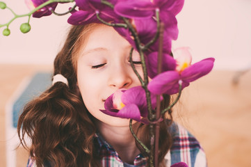 dreamy smiling kid girl smells orchid flower at home