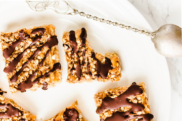 Granola bar cake with date caramel and chocolate. Healthy sweet dessert snack. Cereal granola bar with nuts, fruit and berries on a white marble table. Top view.