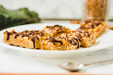 Granola bar with date caramel and chocolate. Healthy sweet dessert snack. Cereal granola bar with nuts, fruit and berries on a white marble table.