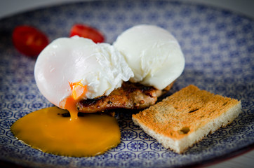 Eggs Benedict with meat steak, tomatoes and toast lying on a blue plate