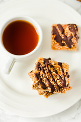 Granola bar with date caramel and chocolate. Healthy sweet dessert snack. Cereal granola bar with nuts, fruit and berries on a white marble table. Top view. A cup of coffee.