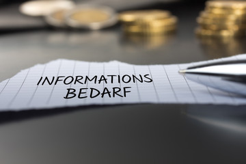 Informationsbedarf auf einem Zettel mit Stift vor Geldmünzen