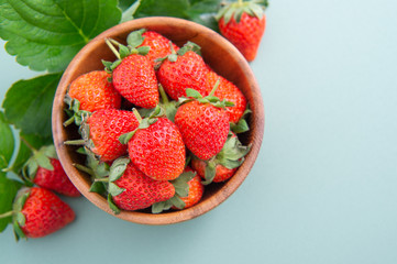 A bowl of beautiful and delicious strawberries isolated on a blue-green background, closeup, topview, copyspace.