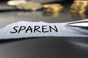 Fototapeta premium Sparen auf einem Zettel mit Stift vor Geldmünzen