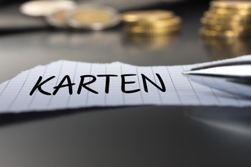 Karten auf einem Zettel mit Stift vor Geldmünzen