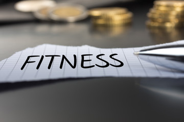 Fitness auf einem Zettel mit Stift vor Geldmünzen