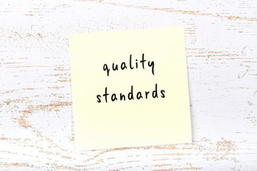 Yellow sticky note with handwritten text quality standards