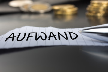 Aufwand auf einem Zettel mit Stift vor Geldmünzen