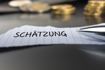 Schätzung auf einem Zettel mit Stift vor Geldmünzen