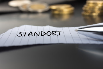 Standort auf einem Zettel mit Stift vor Geldmünzen