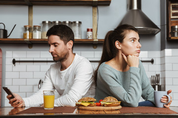 Unhappy young couple sitting at the kitchen