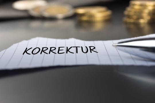 Korrektur auf einem Zettel mit Stift vor Geldm&uuml;nzen