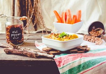 Healthy Homemade Creamy Hummus with with turmeric, green onion and chili paprika in white plate. Served with carrot sticks.Toning.