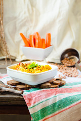 Healthy Homemade Creamy Hummus with with turmeric, green onion and chili paprika in white plate. Served with carrot sticks.Ructic.Space for text.