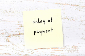 Yellow sticky note with handwritten text delay of payment