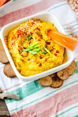 Hummus or houmous, appetizer made of mashed chickpeas with tahini, lemon, garlic, olive oil, parsley and paprika on wooden table.