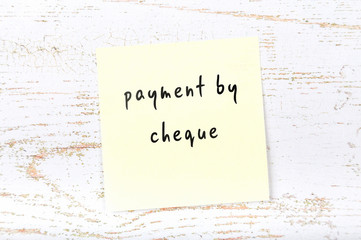 Yellow sticky note with handwritten text payment by cheque