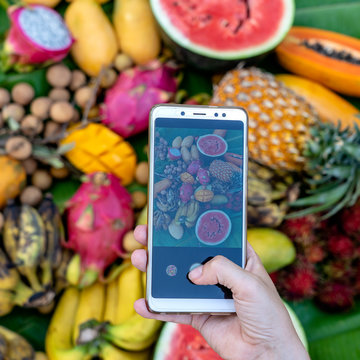 Woman hand take phone photography of tropical fruits. Smartphone photo of breakfast. Sweet mango, papaya, pitahaya, banana, watermelon, pineapple. Raw vegan vegetarian healthy food