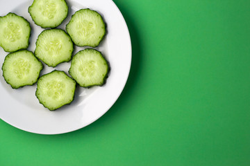 Top view of a plate with sliced cucumber slices on a green background.