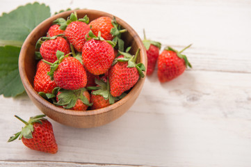 A bowl of beautiful and delicious strawberries isolated on a light wooden background, closeup, topview, copyspace.