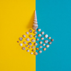 Summer composition in minimal style. Seashell of cone shape with many little seashells on blue and yellow paper background. Flat lay, copy space, top view