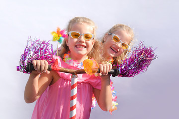 Twin sisters play together riding an imaginative bicycle. They use a rusty handlebar they found in the garage. They fit it with fringes, a windmill and an orange plastic horn.