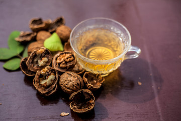 Close up of herbal organic tea of wall nut or walnut tea in a transparent glass cup with raw wall nut in shell and broken also.